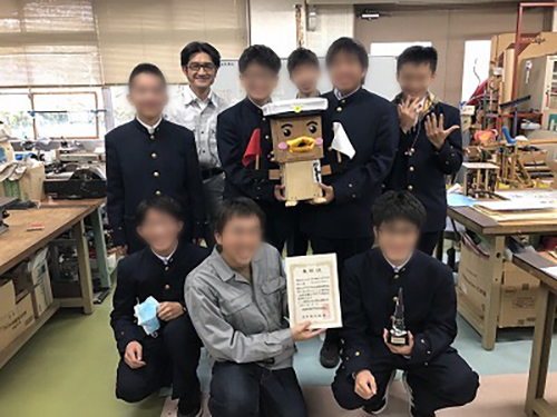 教室にて、賞状を手にした学生や、作成したロボコンを抱えた学生とともに。